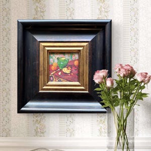 Puede incluir: Una pintura enmarcada que representa una naturaleza muerta con naranjas, un cuenco verde y un cuchillo sobre una mesa. La pintura está en un marco negro con un marco interior dorado. Un ramo de rosas rosas en un jarrón transparente está en primer plano.