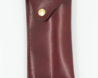 May include: A burgundy leather case with a gold button closure. The case is designed to hold two pens or pencils.