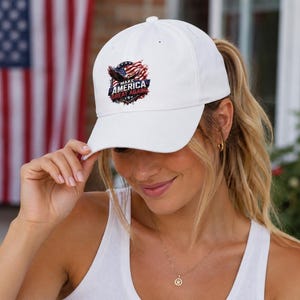 May include: White baseball cap with a curved brim. The cap features a patriotic emblem with an eagle, American flag, and the text "MAKE AMERICA GREAT AGAIN". The cap is worn by a person.
