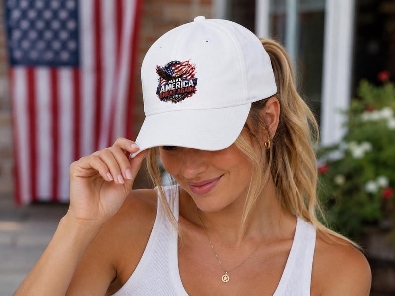 May include: White baseball cap with a curved brim. The cap features a patriotic emblem with an eagle, American flag, and the text "MAKE AMERICA GREAT AGAIN". The cap is worn by a person.
