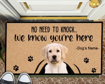 以下が含まれることがあります： 「NO NEED TO KNOCK.. We know you're here」のテキストと、黄色のラブラドールレトリバーの写真がプリントされた長方形のドアマット。足跡と犬の名前を入れるスペースがあります。