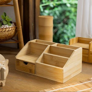 May include: A natural bamboo desk organizer with multiple compartments and a drawer. The organizer is made of light brown bamboo and has a natural wood finish.