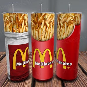 Könnte beinhalten: Drei Edelstahlbecher mit Deckel und Strohhalmen. Jeder Becher hat ein anderes Design mit rotem Hintergrund und einem gelben M-Logo. Die Designs beinhalten eine Tüte Pommes, einen roten Becher mit Pommes und einen roten Becher mit Pommes und dem Text "McDiabetes".