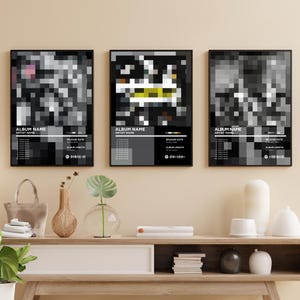 Puede incluir: Tres impresiones artísticas enmarcadas con diseños abstractos pixelados en blanco, negro y gris. Cada impresión incluye texto en la parte inferior con "Album Name" y "Artist Name". Las impresiones se exhiben en una consola de madera.