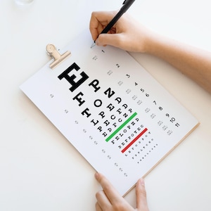 Può includere: Un tabellone bianco per la vista con lettere nere è tenuto su un appoggio di legno. Una mano che tiene una penna scrive sul tabellone. Il tabellone ha linee verdi e rosse che evidenziano righe specifiche di lettere.
