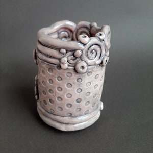 May include: A small, pink ceramic planter with a textured, dotted surface and a decorative, swirling rim.