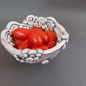 May include: A white ceramic bowl with a textured, organic design, filled with small red tomatoes.