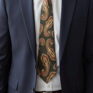 May include: A navy blue suit with a white dress shirt and a paisley patterned tie. The tie features a dark green background with red, gold, and white accents. A brown leather belt is visible.