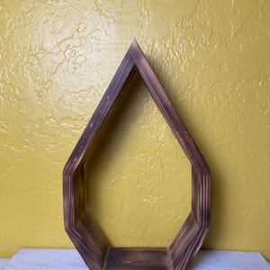 May include: A dark brown wooden shelf shaped like a teardrop. The shelf is mounted on a white wall.