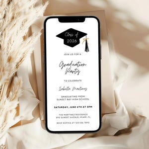 May include: A smartphone displays a graduation party invitation. The invitation features a black graduation cap graphic with the text "Class of 2026." The invitation text reads "Graduation Party" and includes event details such as the date, time, and location.