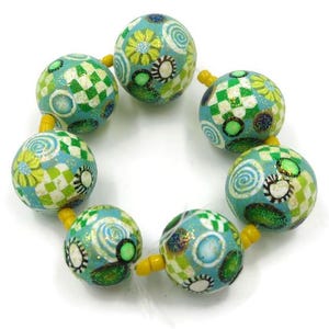 May include: A beaded bracelet featuring round, patterned beads in shades of teal, green, and yellow. The beads have floral, checkered, and swirl designs. The bracelet is strung on a yellow cord, creating a colorful accessory.