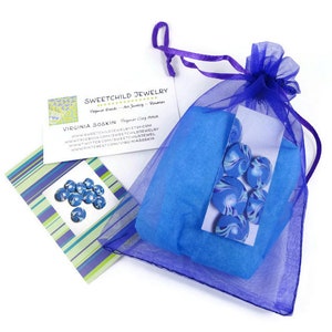 May include: A blue and white swirl polymer clay bead set in a purple organza bag. The bag is tied with a purple ribbon. The beads are packaged with a business card that reads "Sweetchild Jewelry" and "Virginia Soskin Polymer Clay Artist".