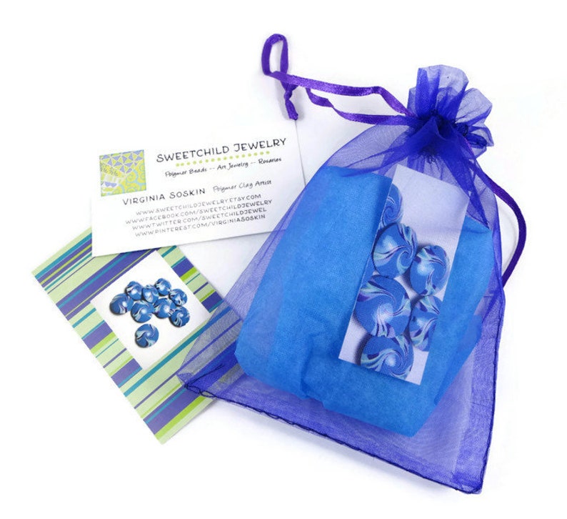 May include: A blue and white swirl polymer clay bead set in a purple organza bag. The bag is tied with a purple ribbon. The beads are packaged with a business card that reads "Sweetchild Jewelry" and "Virginia Soskin Polymer Clay Artist".