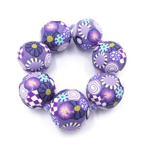 May include: A purple and white patterned bracelet made of round beads. The beads have a floral and geometric design.