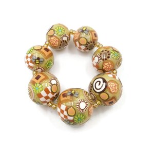 May include: A handmade bracelet featuring large, round beads in shades of tan, brown, and gold. The beads are decorated with floral, geometric, and insect patterns. The bracelet is strung on a gold-colored cord.