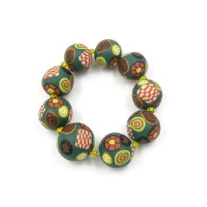 May include: A beaded bracelet featuring dark green, round beads with various patterns. The patterns include red and white checkered designs, brown stars, and yellow and brown floral and swirl motifs. The beads are strung together with gold-colored string.
