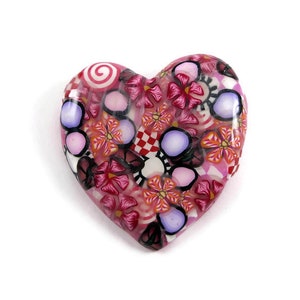 May include: A pink heart-shaped pendant with a colorful floral pattern. The pattern includes pink, red, white, and purple flowers, as well as swirls and polka dots.
