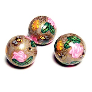 May include: Three round, gray glass beads with a gold glitter finish. Each bead is decorated with a floral pattern of pink and yellow roses, green leaves, and small black bees.