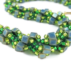 May include: A close-up of a green and blue beaded bracelet. The bracelet is made with small, square beads in a woven pattern.