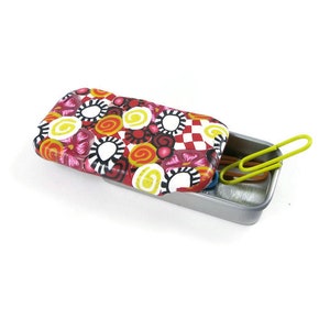 May include: A small, rectangular tin with a colourful, patterned lid. The lid is open and reveals a silver interior with a few paper clips inside.
