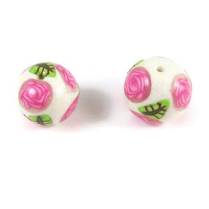 May include: Two white round beads with pink roses and green leaves printed on them.
