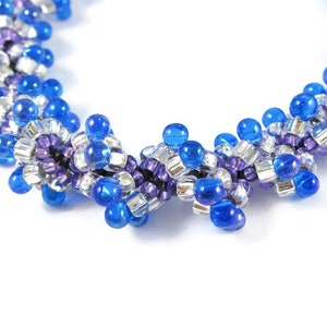 May include: A close-up of a beaded bracelet with a spiral design. The bracelet is made with blue, silver, and purple beads.