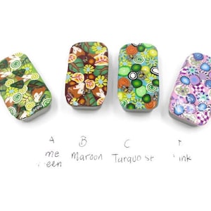 May include: Four small rectangular tins with different colourful patterned designs. The tins are labelled A, B, C, and D. A is labelled "me green", B is labelled "maroon", C is labelled "Turquoise", and D is labelled "ink".