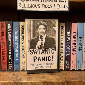 May include: A shelf of VHS tapes with a sign reading "SENSATIONAL! RELIGIOUS DOCS & CULTS." The central tape is labeled "SATANIC PANIC! THE GERALDO RIVERA SPECIAL - 1988." Other tapes include "HELLFIRE & HEAVY METAL" and "CARE BEARS."