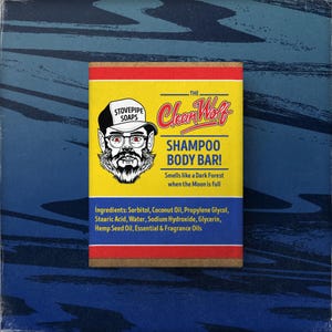 May include: A yellow and red shampoo and body bar with the text "The Clean Wolf" and "Shampoo Body Bar!". The bar features a cartoon illustration of a man with glasses and a beard. The bar smells like a dark forest.