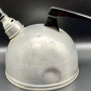 May include: A silver aluminum kettle with a black plastic handle. The kettle has a rounded body and a spout on the side.
