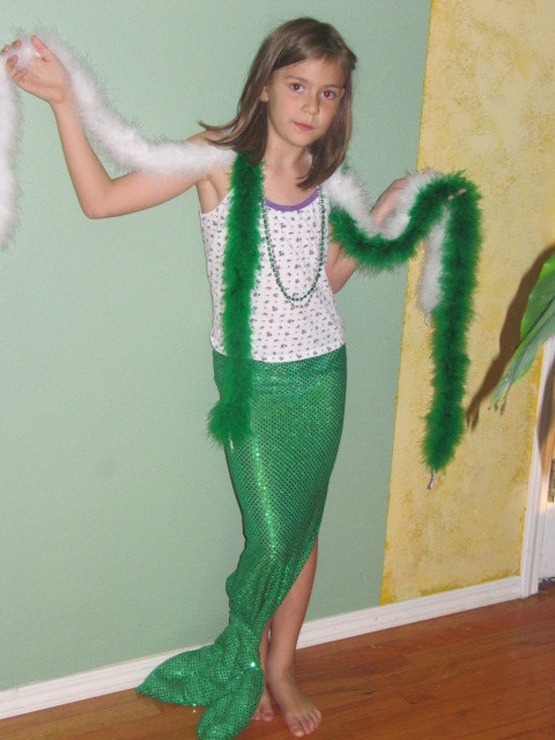 Puede incluir: Una ni&ntilde;a peque&ntilde;a con un disfraz de cola de sirena verde y un boa de plumas blanco y verde. Est&aacute; sosteniendo un boa de plumas blanco en su mano izquierda.
