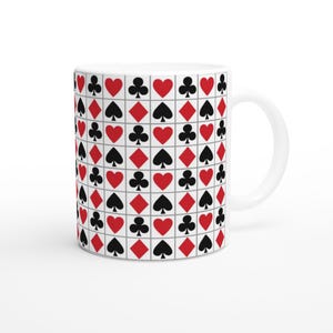 May include: White ceramic mug featuring a repeating pattern of playing card suits: hearts, diamonds, clubs, and spades. The suits are in red and black, set against a grid of white squares. The mug has a curved handle.