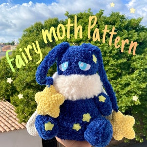 Peut inclure: Un jouet en peluche de fée papillon bleu crocheté avec des accents d'étoiles jaunes. Le jouet a un ventre blanc moelleux et des yeux bleus. Le texte "fairy moth pattern" est écrit en jaune en haut de l'image.