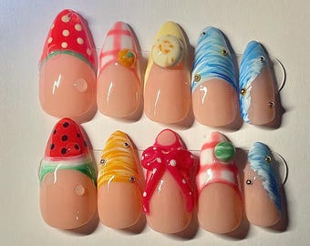 May include: A set of ten artificial nails with various designs. The nails feature a light pink base with colorful accents, including polka dots, stripes, and fruit-themed decorations. Some nails have small, decorative embellishments.
