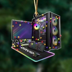 May include: A gaming PC ornament with a monitor, keyboard, mouse, and headset. The black PC case has colorful lights, as does the monitor. The mousepad says "DAVID". The ornament is decorated with string lights.