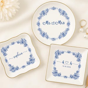 May include: Three white ceramic ring dishes with gold rims. Each dish features a blue floral wreath design. One dish has "Mr & Mrs" text, another has "Sophia" text, and the third has "h & b" and the date "10.18.2025".
