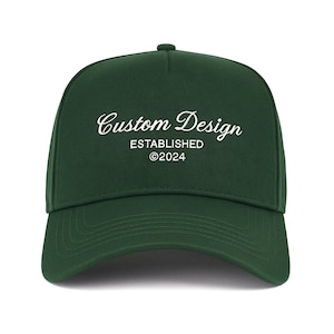 May include: A dark green trucker hat with white embroidered text that reads "Custom Design Established ©2024".