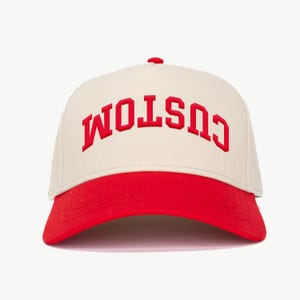 May include: A beige and red baseball cap with the word "CUSTOM" embroidered in red on the front.