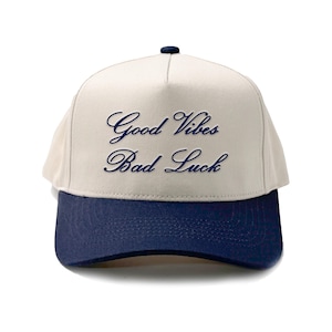 Könnte beinhalten: Eine beige und marineblaue Baseballkappe mit dem Schriftzug "Good Vibes Bad Luck", der in Marineblau gestickt ist.