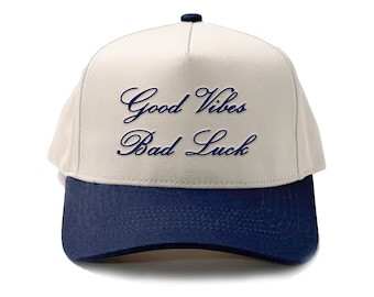 Könnte beinhalten: Eine beige und marineblaue Baseballkappe mit dem Schriftzug "Good Vibes Bad Luck", der in Marineblau gestickt ist.