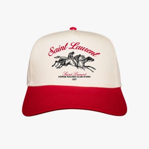 Puede incluir: Una gorra de béisbol blanca y roja con una imagen en blanco y negro de caballos y jinetes. La gorra tiene el texto "Saint Laurent Horse Racing Club ©1984 007" en rojo.