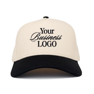 May include: A cream-coloured baseball cap with a black brim and a black button on top. The front of the cap features the black embroidered text "Your Business LOGO" with "Your" and "Business" in a script font and "LOGO" in a bold serif font.