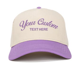 Könnte beinhalten: Eine beige und lilafarbene Baseballkappe mit dem Text "Your Custom Text Here" in lilafarbener Kursivschrift.