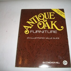 May include: A brown book with a yellow title that reads "Antique Oak Furniture: An Illustrated Value Guide" by Conover Hill. The book cover features a wood grain pattern and the price is $7.95.
