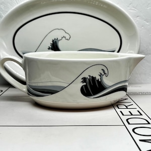 May include: White ceramic gravy boat and oval serving platter with a black and grey wave design. The gravy boat has a handle and a spout. The platter and gravy boat are part of a matching set.
