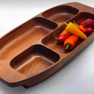 May include: A rectangular wooden serving tray with four distinct recessed compartments of varying sizes. The tray features a rich brown wood grain finish. Several small, fresh bell peppers in vibrant shades of red, orange, and yellow are placed inside one of the larger sections.