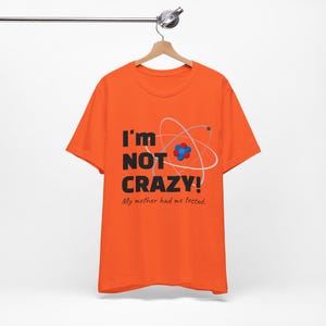 May include: Orange t-shirt with a black graphic that says "I'm not crazy! My mother had me tested." and a stylised atom illustration.
