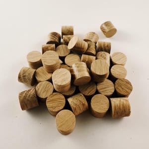 以下が含まれることがあります： 薄い茶色の丸い木製のダボが積み重ねられています。ダボの直径は約2.5cmで、ランダムなパターンで配置されています。