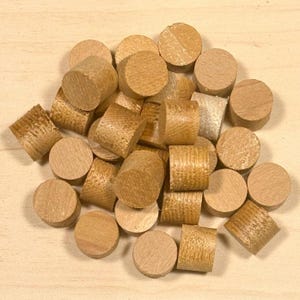 May include: A collection of small, cylindrical wooden plugs in various shapes and sizes. Some have flat, circular tops, while others have textured, ridged sides. The plugs are a light brown color and appear to be made of hardwood.