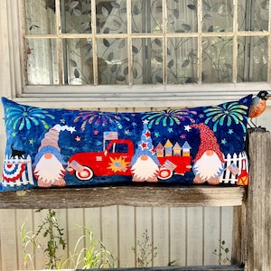 Könnte beinhalten: Ein langes, rechteckiges Kissen mit blauem Hintergrund und einem rot-weiß-blauen patriotischen Thema. Das Kissen zeigt Gnome, einen roten LKW, Feuerwerk und Sterne.